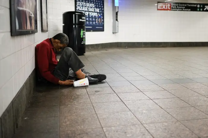 A person sits on the floor of a subway station.